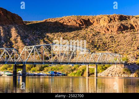 Eine Brücke überspannt einen Fluss mit Blick auf die Berge im Hintergrund. Die Brücke besteht aus Metall und ist von Wasser umgeben Stockfoto