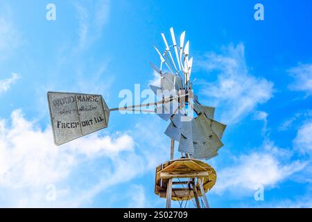Eine Windmühle mit den Worten 'Dünger' drauf. Die Windmühle steht auf einem Pfosten und ist von einem blauen Himmel umgeben Stockfoto