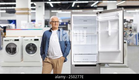 Ein reifer Mann lehnt sich auf einen Kühlschrank im Elektrogerätegeschäft Stockfoto