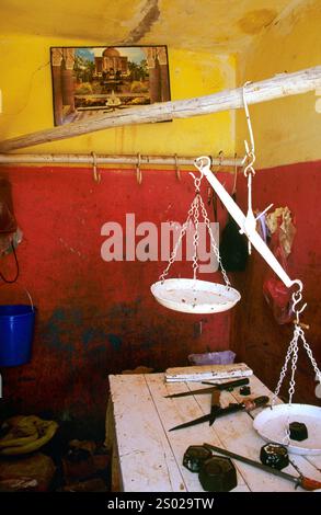 Rustikale Metzgerei in Marokko mit traditioneller Waage, Gewichten, Messern und leuchtenden gelben und roten Wänden in ländlicher Umgebung. Stockfoto