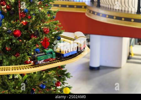 Ein entzückender und charmanter Miniaturzug schlingt elegant um einen wunderschön geschmückten Weihnachtsbaum Stockfoto