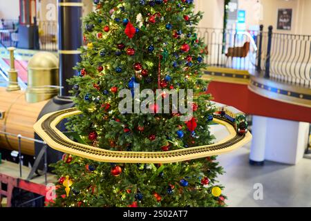 Ein wunderschön und festlich geschmückter Weihnachtsbaum mit einem bezaubernden Modellzug, der fröhlich um ihn kreist Stockfoto