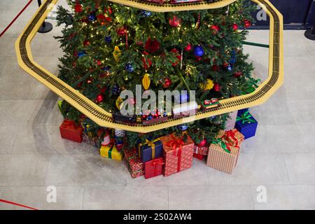 Ein wunderschön dekorierter Weihnachtsbaum, der elegant mit bunten Geschenken und einer bezaubernden Spielzeugbahn verziert ist Stockfoto