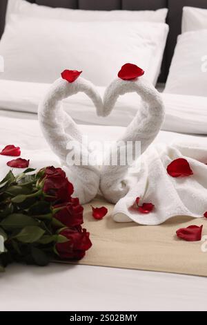 Flitterwochen. Schwäne aus Handtüchern und wunderschöne rote Rosen auf dem Bett Stockfoto