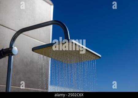 Nahaufnahme einer Außendusche mit fließendem Wasser vor einem hellblauen Himmel und einer modernen Gebäudekulisse. Stockfoto