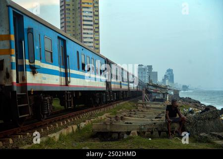 Colombo. Dezember 2024. Dieses Foto vom 18. Dezember 2024 zeigt einen Zug am Meer in Colombo, Sri Lanka. Die Küstenbahnlinie an der Westküste Sri Lankas und in der Nähe des Indischen Ozeans ist eine wichtige Eisenbahnlinie in diesem Inselstaat. Es ist auch eine berühmte Touristenattraktion, wo die geradlinige Küste, die Kutschen ohne Türen und der wunderschöne Meerblick während der gesamten Reise den Menschen ermöglichen, das einzigartige Erlebnis im Ceylon-Stil zu erleben. Quelle: Gayan Sameera/Xinhua/Alamy Live News Stockfoto