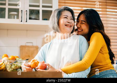 Eine schürzenbekleidete junge asiatische Frau und ihre alte Mutter verbinden sich mit Essen und Getränken in der Küche. Ihre Stockfoto