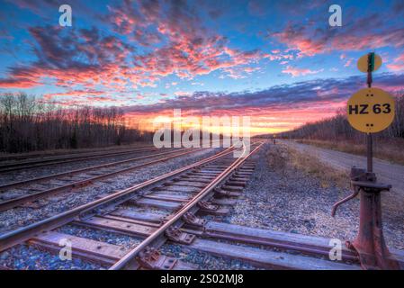 Ein Zuggleis mit einem Schild mit der Aufschrift HZ 63. Der Himmel ist orange und rosa, und die Gleise sind leer Stockfoto