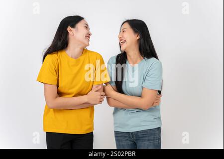 Zwei fröhliche, lebendige asiatische Freundinnen in lässiger Kleidung stehen vor weißem Studiohintergrund und genießen es, gemeinsam zu reden und zu lachen. Am besten f Stockfoto