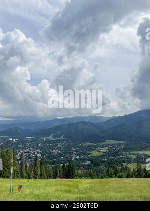 Blick auf die Berge mit bewachsenem Gras und Bäumen, die Stadt ist in der Ferne sichtbar. Tatra - Polen Stockfoto