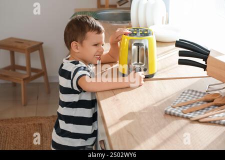 Süßer kleiner Junge, der Toaster auf der Theke in der Küche dreht. Gefährdetes Kind Stockfoto