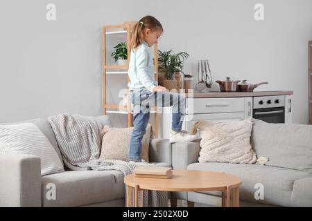 Niedliches kleines Mädchen, das zu Hause auf Sofas läuft. Kind in Gefahr Stockfoto