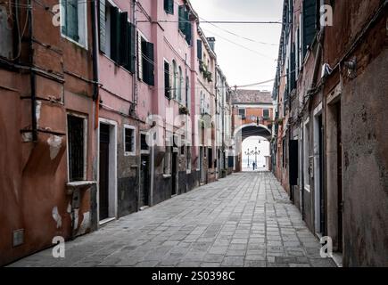 Eine ruhige, enge Straße in einer historischen italienischen Stadt, gesäumt von bunten Gebäuden und Kopfsteinpflaster. Die Szene zeigt einen Bogengang in der Distanz Stockfoto