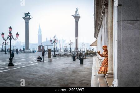 Eine ruhige Szene in Venedig, Italien, mit leeren Cafés im Freien, historischen Säulen und einem Darsteller in einem goldenen Kostüm. Die Atmosphäre ist nebelig und heiter Stockfoto