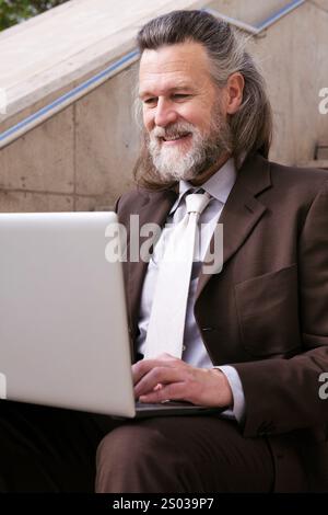 Mann sitzt auf einer Treppe und arbeitet online auf einem Laptop Stockfoto