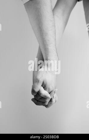 Zwei Hände in der Hand vor neutralem Hintergrund gehalten. Nahaufnahme der Hand von Mann und Frau. Konzept von Intimität, Unterstützung und Vertrauen. Schwarzweißbild. Stockfoto