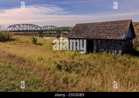 Eine Brücke und eine kleine Kabine werden in einem Feld gezeigt. Die Brücke ist grün und erstreckt sich über ein Gewässer. Die Hütte ist alt und aus Holz. Die Szene ist Stockfoto