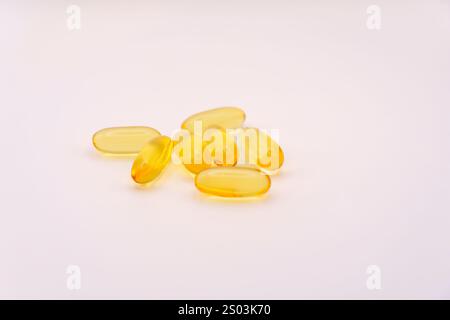 Gruppe von gelben Omega-3-Softgel-Kapseln, die auf einem sauberen weißen Hintergrund angeordnet sind und ihre durchscheinende Textur und leuchtende Farbe zeigen. Stockfoto