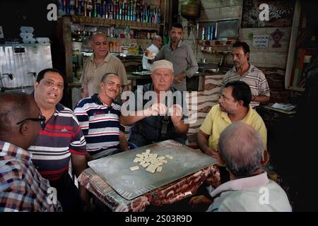 Ein lebhaftes Treffen ägyptischer Männer, die Dominospiele spielen und Tee in einem traditionellen Café in Alexandria, Ägypten, genießen. Die Szene spiegelt Kameradschaft wider Stockfoto