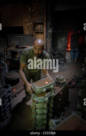 Ein Gießereiarbeiter, der eine Form in einer Metallwerkstatt in Alexandria, Ägypten, akribisch bearbeitet. Die Szene zeigt traditionelle Handwerkskunst . Stockfoto