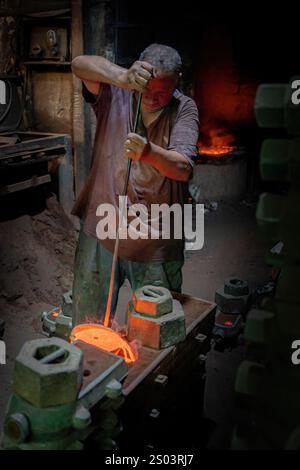 Ein Gießereiarbeiter in einer Werkstatt in Alexandria, Ägypten, der geschmolzenes Metall während eines Gießprozesses gekonnt handhabte. Ein großes Gründerbild Stockfoto