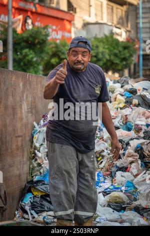 Ein engagierter Müllsammler in Alexandria, Ägypten, stellt sich inmitten von Müllhaufen auf die Daumen und zeigt Widerstandsfähigkeit und harte Arbeit, städtisches Leben. Stockfoto