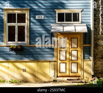 Ein bezauberndes blaues Holzhaus mit gelber Tür und weißer Zierleiste. Das Haus verfügt über zwei Fenster, eine kleine Markise über der Tür und einen Blumenkasten darunter Stockfoto