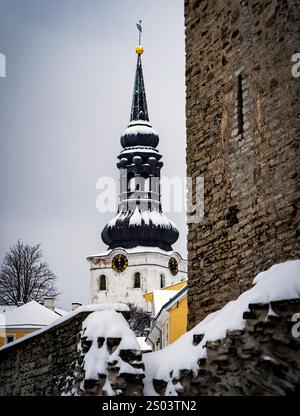 Eine schneebedeckte Szene mit einem historischen Kirchturm mit einer markanten schwarzen Kuppel und einem Turm, umgeben von alten Steinmauern. Der Himmel ist bedeckt Stockfoto