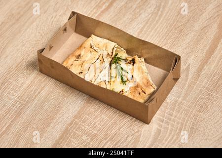 Eine Take-away-Box mit gebackenem Fladenbrot mit geschmolzenem Käse und Rosmarin. Stockfoto