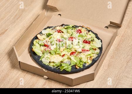 Eine einzigartige Pizza mit schwarzem Teig, garniert mit Huhn, Salat, Tomaten und Parmesan. Stockfoto