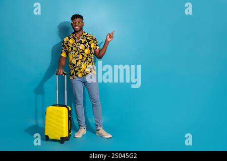 Stilvoller junger Mann mit einem Koffer auf blauem Hintergrund, der Reisefreude verkörpert Stockfoto