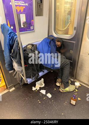 Ein ungepflegter Obdachloser schläft in einem New Yorker U-Bahn-Auto, auf dem Boden liegen die Reste einer Mahlzeit. Stockfoto