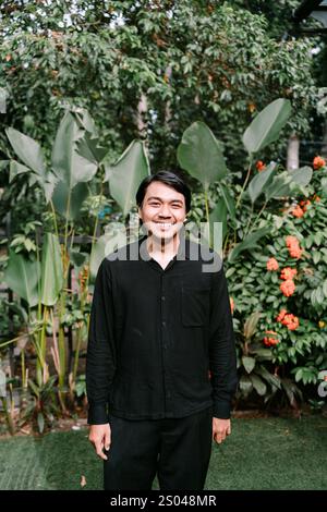 Ein südostasiatischer Mann, der warm lächelt, während er geradeaus blickt und einen fröhlichen und freundlichen Ausdruck ausstrahlt Stockfoto