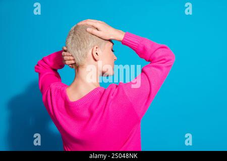Eine junge Frau mit kurzen blonden Haaren posiert vor einem leuchtend blauen Hintergrund und trägt einen stylischen, leuchtend rosa Pullover. Stockfoto