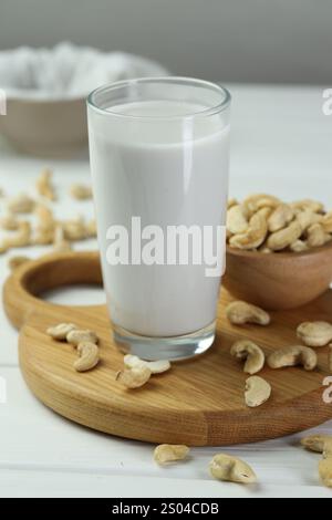 Frische Cashew-Milch im Glas und Nüsse auf weißem Holztisch, Nahaufnahme Stockfoto