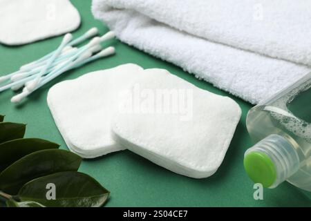 Wattepads, Tupfer, Kosmetikartikel, Handtuch und Blätter auf grünem Hintergrund, Nahaufnahme Stockfoto