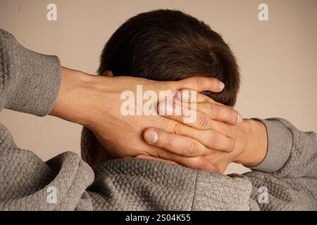 Nahaufnahme von gefalteten Händen auf dem Hinterkopf eines Mannes. Das minimalistische Ambiente betont die symbolische Bedeutung der Einheit und des Zusammenspiels der Geste Stockfoto