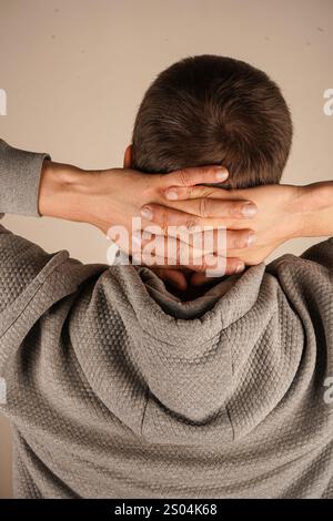 Der isolierte Hintergrund unterstreicht sein beiläufiges, friedliches Verhalten. Ein Mann in einem Hoodie schließt seine Hände hinter den Kopf und dehnt sich in einer entspannten Haltung. Stockfoto