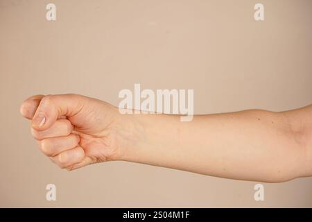 Eine hochgezogene geballte Faust hebt sich von einer hellen Wand ab und symbolisiert Stärke und innere Stärke. Der neutrale Hintergrund lenkt die Aufmerksamkeit auf den Entscheid Stockfoto