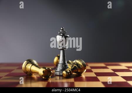 Silberner Schachkönig zwischen gefallenen goldenen Stücken auf Schachbrett vor grauem Hintergrund, Nahaufnahme. Wettbewerbskonzept Stockfoto