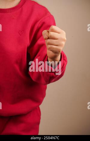 Eine hochgezogene geballte Faust hebt sich von einer hellen Wand ab und symbolisiert Stärke und innere Stärke. Der neutrale Hintergrund lenkt die Aufmerksamkeit auf den Entscheid Stockfoto