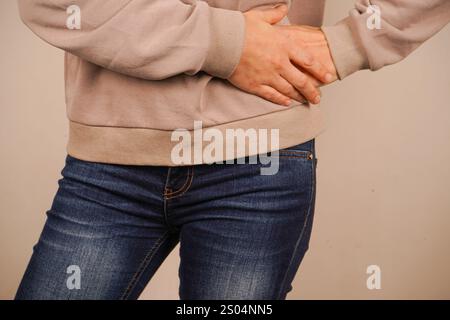 Eine Hand wird auf die andere gelegt. Die Frau legt ihre Hände unter ihre Rippen. Ihre Hände werden an ihren Körper gehalten, als ob sie die Schmerzlinderung vermitteln würden Stockfoto