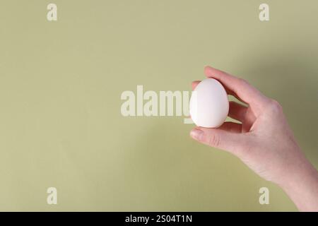 Frau, die rohes Ei auf Oliven-Hintergrund hält, Nahaufnahme. Leerzeichen für Text Stockfoto