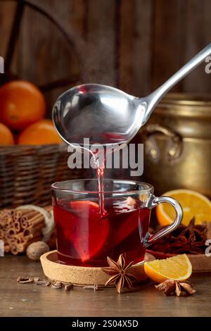 Glühwein wird in einen Glasbecher gegossen. Glühwein mit Zutaten auf einem alten Holztisch. Stockfoto