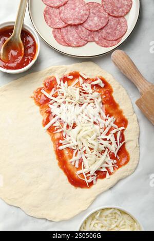 Zubereitung von Calzone-Pizza. Teig mit Soße, Käse und anderen Zutaten auf dem Tisch, flach gelegt Stockfoto