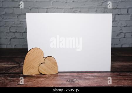 Hölzerne Herzen zusammen mit einer leeren Karte auf einem Holztisch Stockfoto