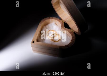 Goldene Eheringe in einer herzförmigen Holzkiste mit dramatischer Beleuchtung Stockfoto