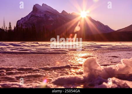 Ein wunderschöner Sonnenuntergang über einem See mit Bergen im Hintergrund. Die Sonne scheint hell und schafft eine warme und friedliche Atmosphäre Stockfoto