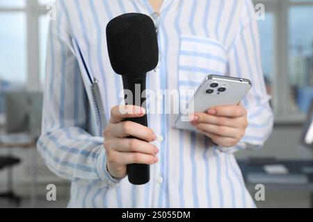 Journalist mit Mikrofon und Smartphone drinnen, Nahaufnahme Stockfoto