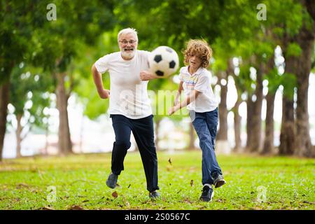 Großvater und Kinder spielen Fußball im sonnigen Park. Glückliche Familie beim Ball. Opa und Kinder spielen Fußball. Die Liebe der Generation. Aktiver Senior-Mann Stockfoto